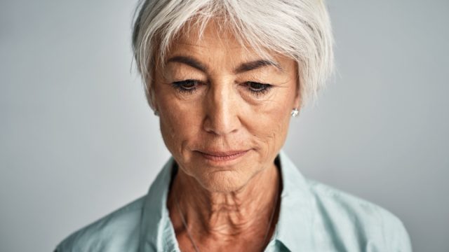 Senior woman posing against a grey background.