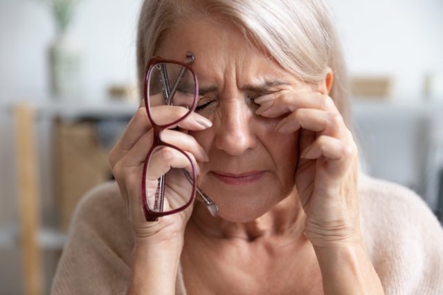 A mature woman takes off her glasses and massages her eyes.