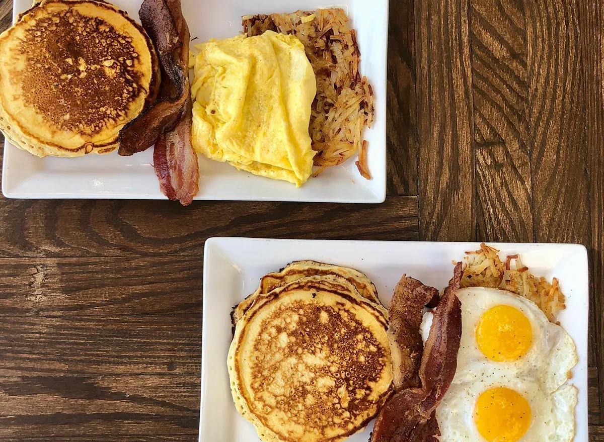 two plates of pancakes with eggs and bacon