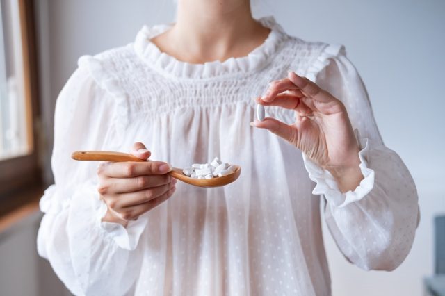 Woman in white blouse holding in hand wooden spoon with suplement.