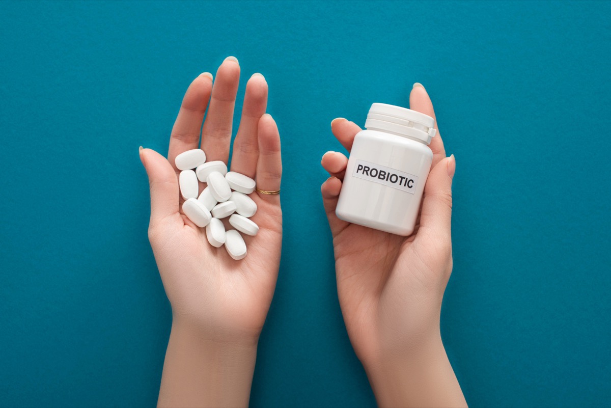 Woman holding white probiotic container and pills in hands.