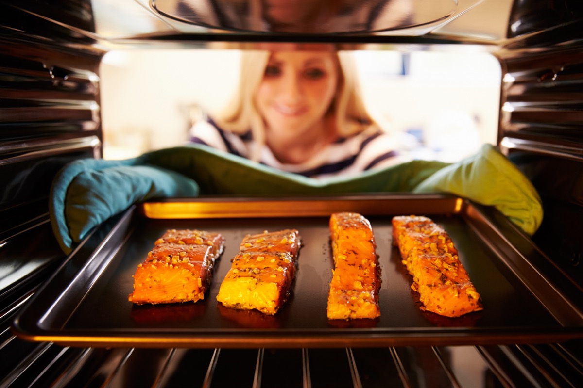 woman removing baking sheet with salmon from oven