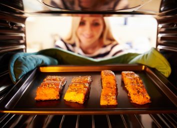 woman removing baking sheet with salmon from oven