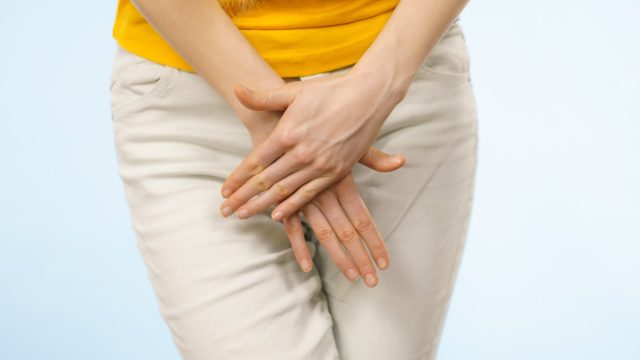 A woman with hands holding pressing her crotch lower abdome.,