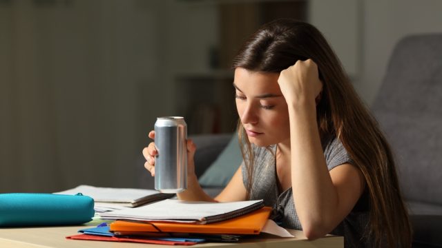 young woman drinking energy drink while studying