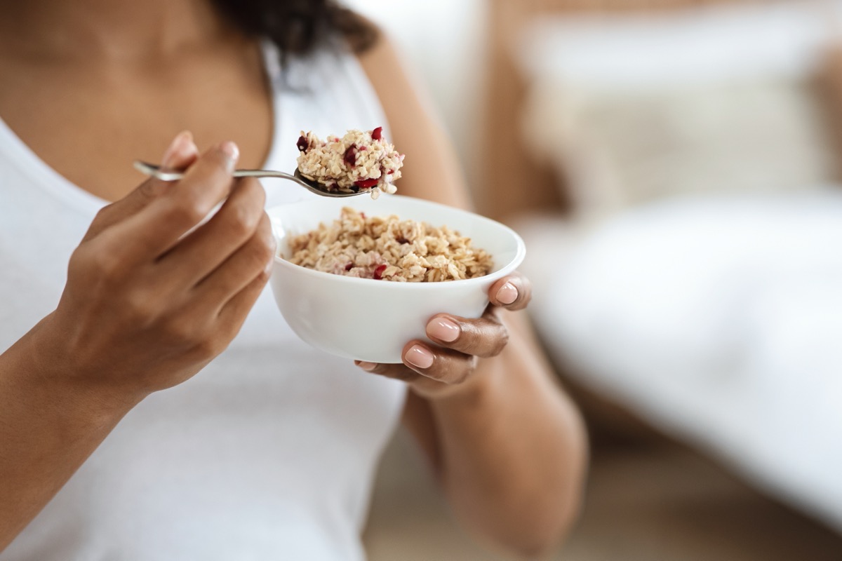 young woman eating oatmeal with cranberries out of a white bowl
