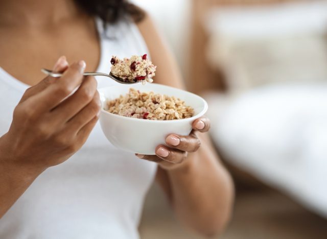 young woman eating oatmeal with cranberries out of a white bowl