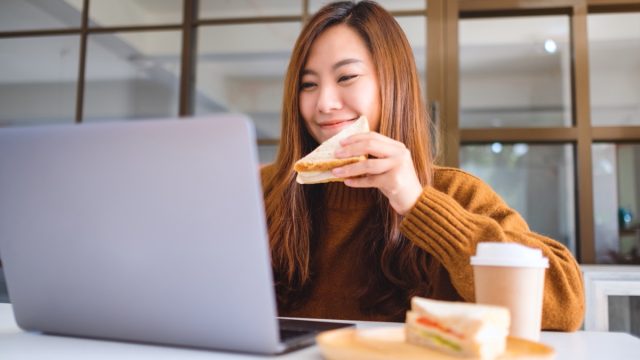 woman eating sandwich while sitting at laptop