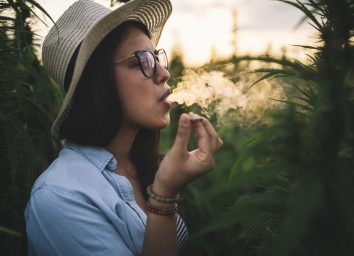 Woman with hat smoking joint in marijuana plantation at sunset.