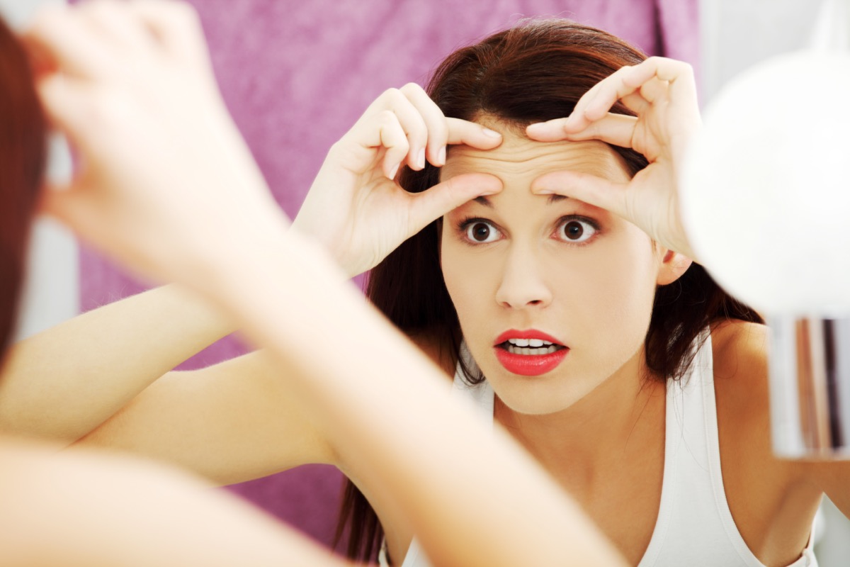 Mirror reflection of a woman worrying because of wrinkles on her forehead.