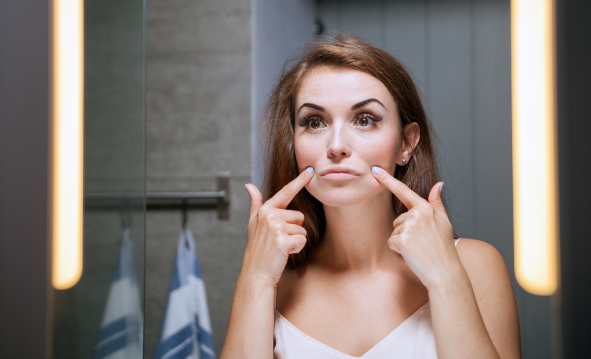 Young woman checking wrinkles on face in front of a bathroom mirror