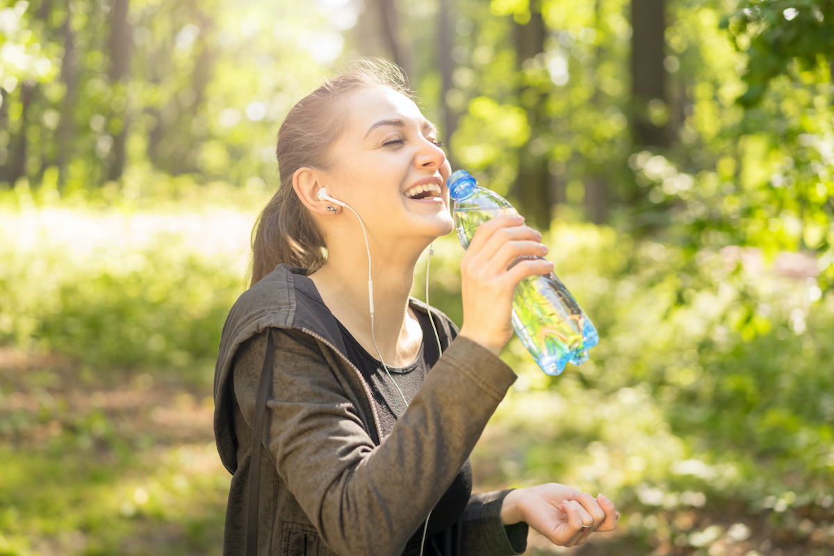Sport laughing young woman in the sunny park with bottle of water and headphones, happy, sport, healthy concept