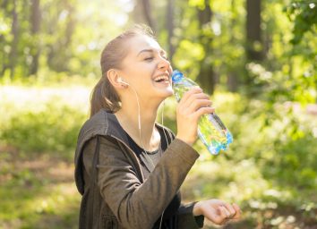 Sport laughing young woman in the sunny park with bottle of water and headphones, happy, sport, healthy concept
