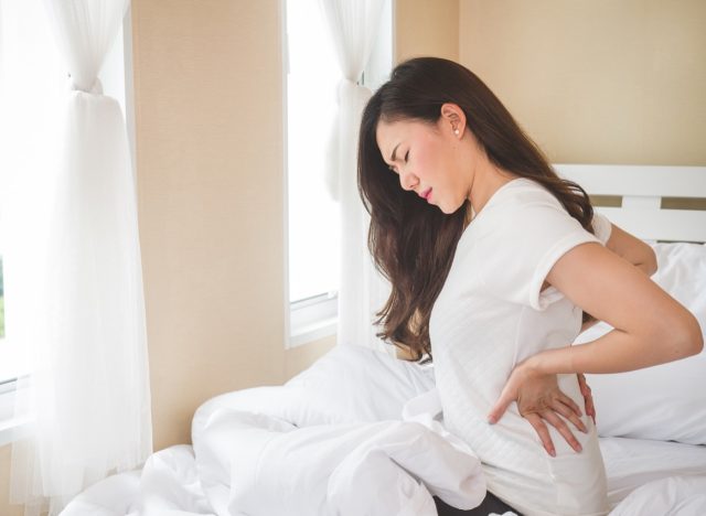 young woman sitting in bed with back ache or kidney pain