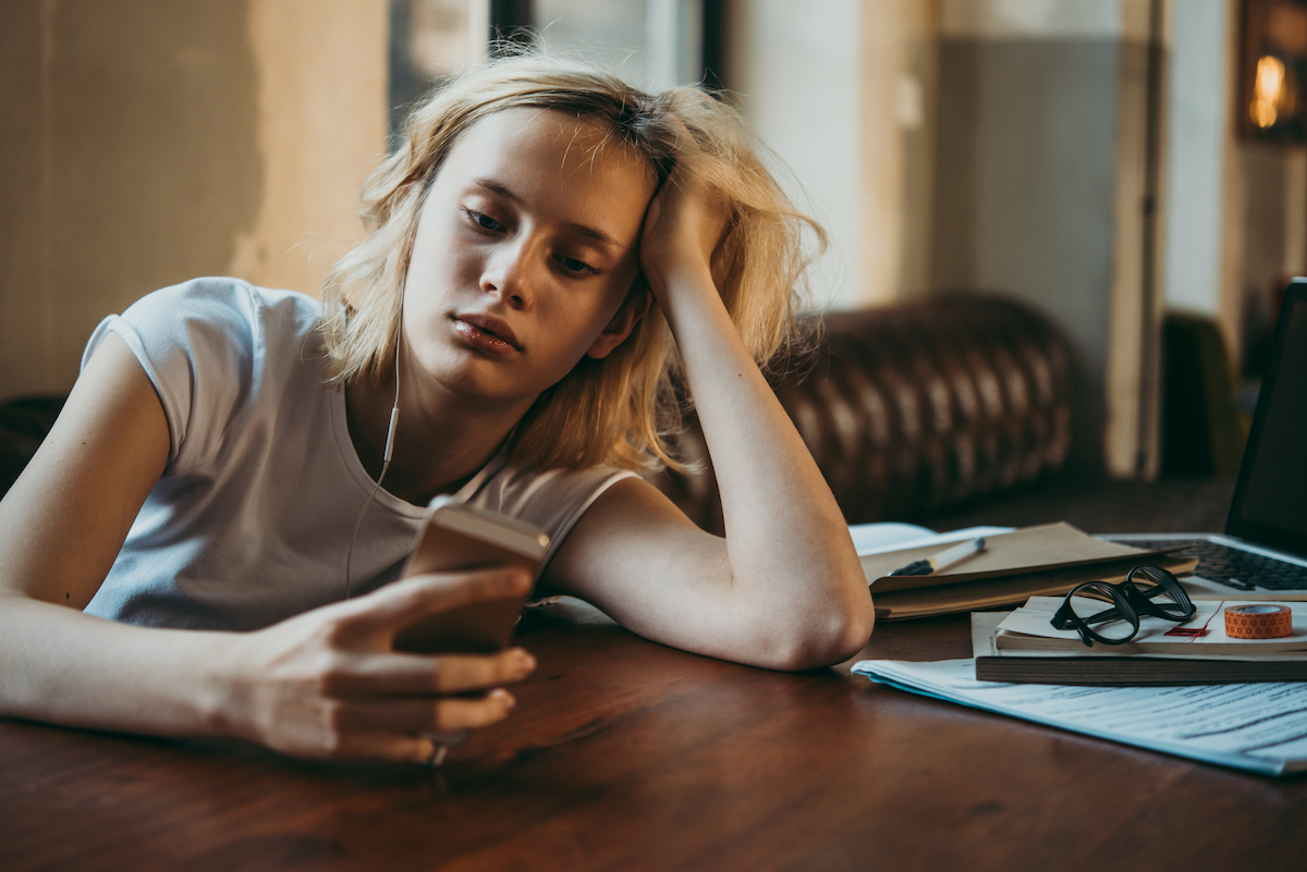 A teenage girl listening to music and looking at her smartphone. Procrastination and laziness concept