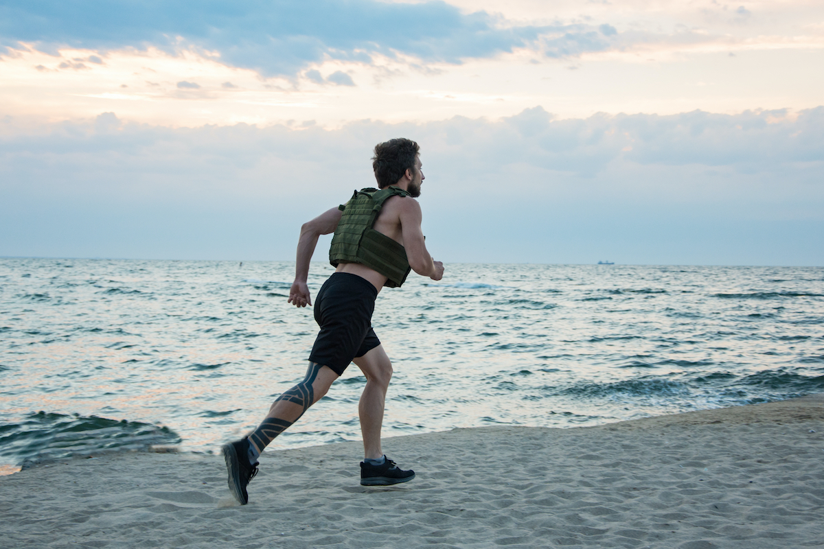 Young bearded athlete training outdoor with weighted vest, exercise with military plate carrier