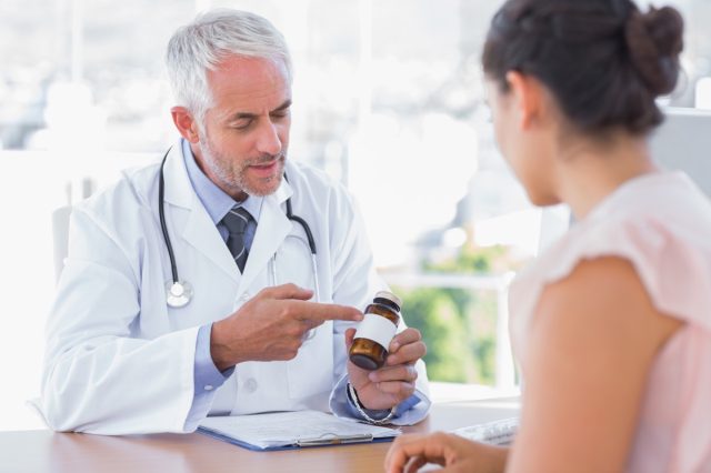 Doctor explaining the bottle of pills to patient in the office at desk