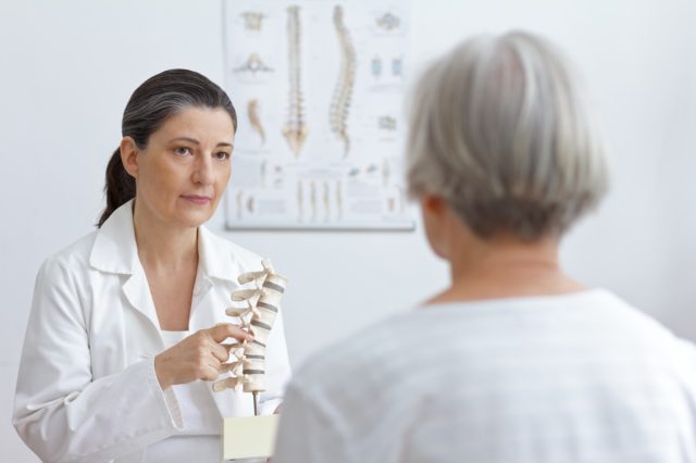 Orthopedic doctor showing senior patient a hernia on a spine model.