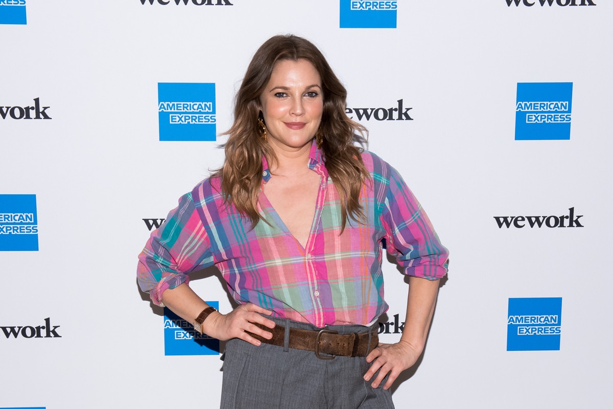 drew barrymore in pink plaid shirt standing in front of amex step-and-repeat