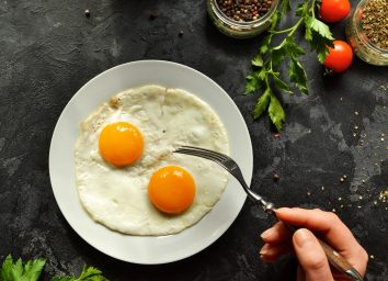 person eating two eggs off a white plate