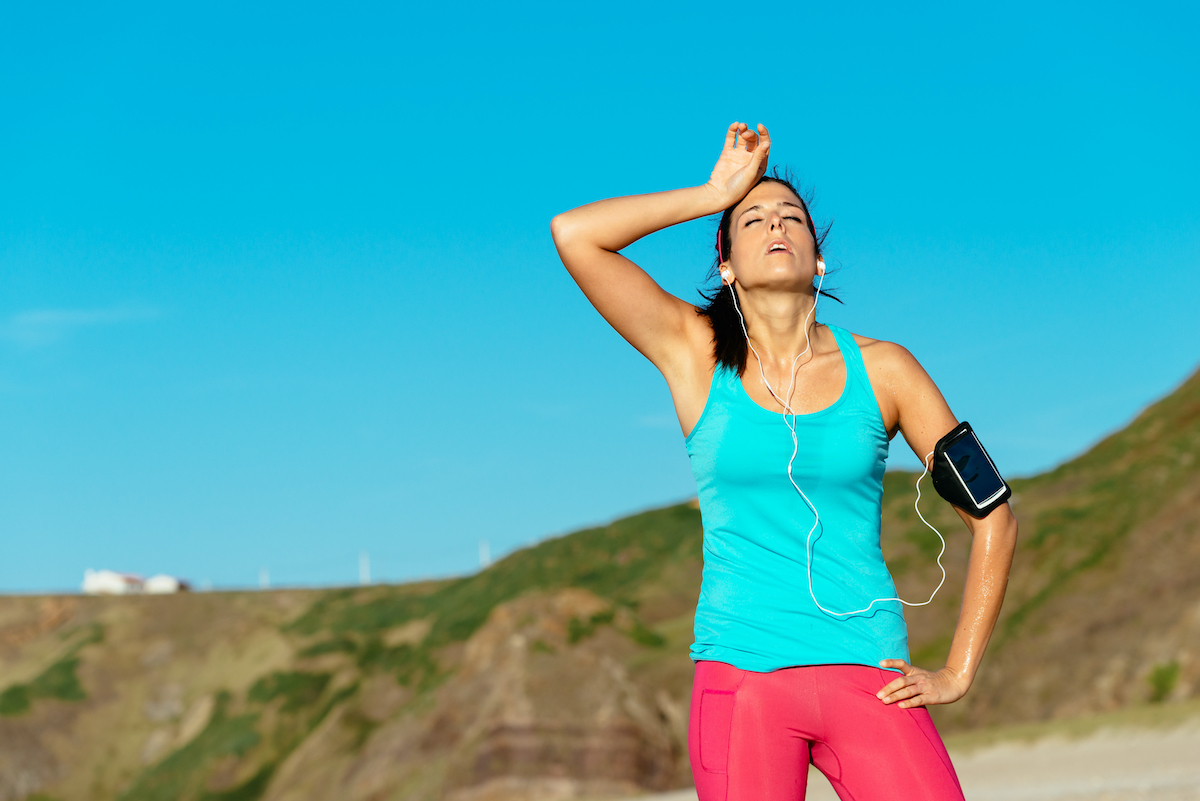 Exhausted female runner overtraining and sweating after training on hot summer at beach. Fitness sweaty woman on workout.