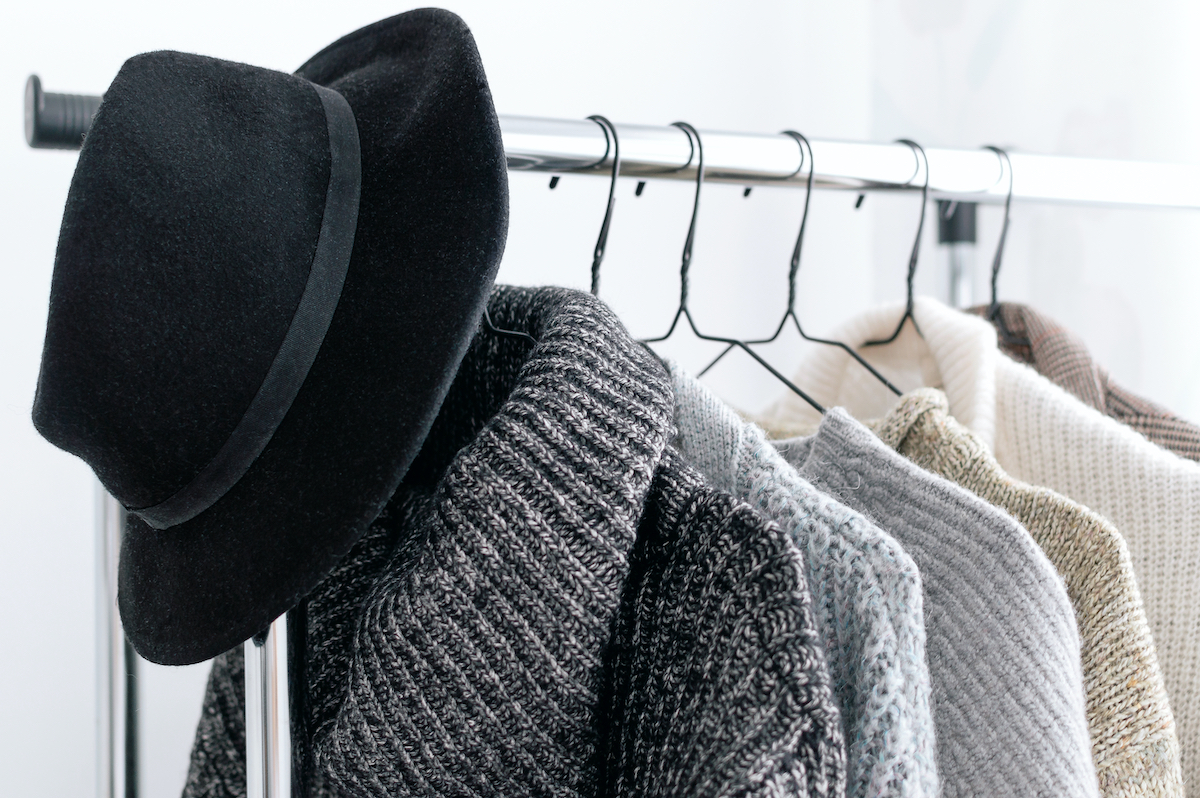Winter wardrobe showcase. White and gray tone knitwear and hat hanging on a clothes rack. Selective focus, horizontal