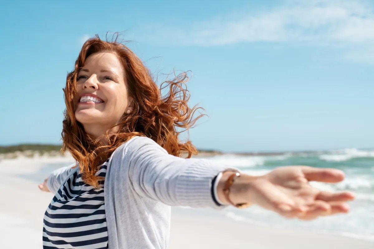 Happy mature woman with arms outstretched feeling the breeze at beach.