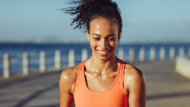 Smiling young female runner taking a breather. Healthy young woman with sweat standing on the promenade after her workout and smiling.