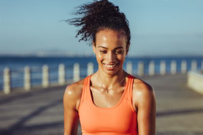 Smiling young female runner taking a breather. Healthy young woman with sweat standing on the promenade after her workout and smiling.