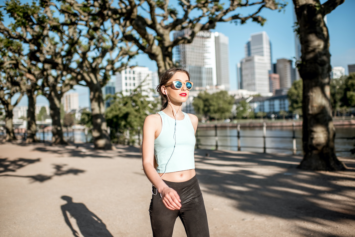 Young woman in sportswear having a morning exercise walking in the park with skyscrapers on the background in Frankfurt city