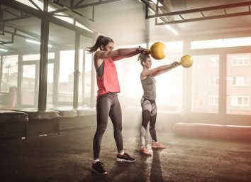 Two woman lifting kettle bell in cross fit gym