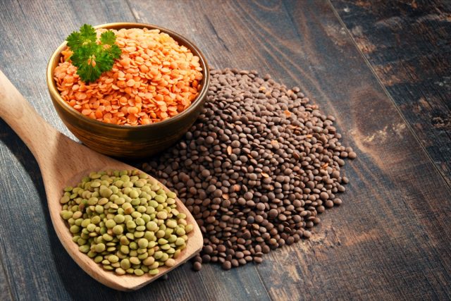 Composition with bowl of lentils on wooden table.