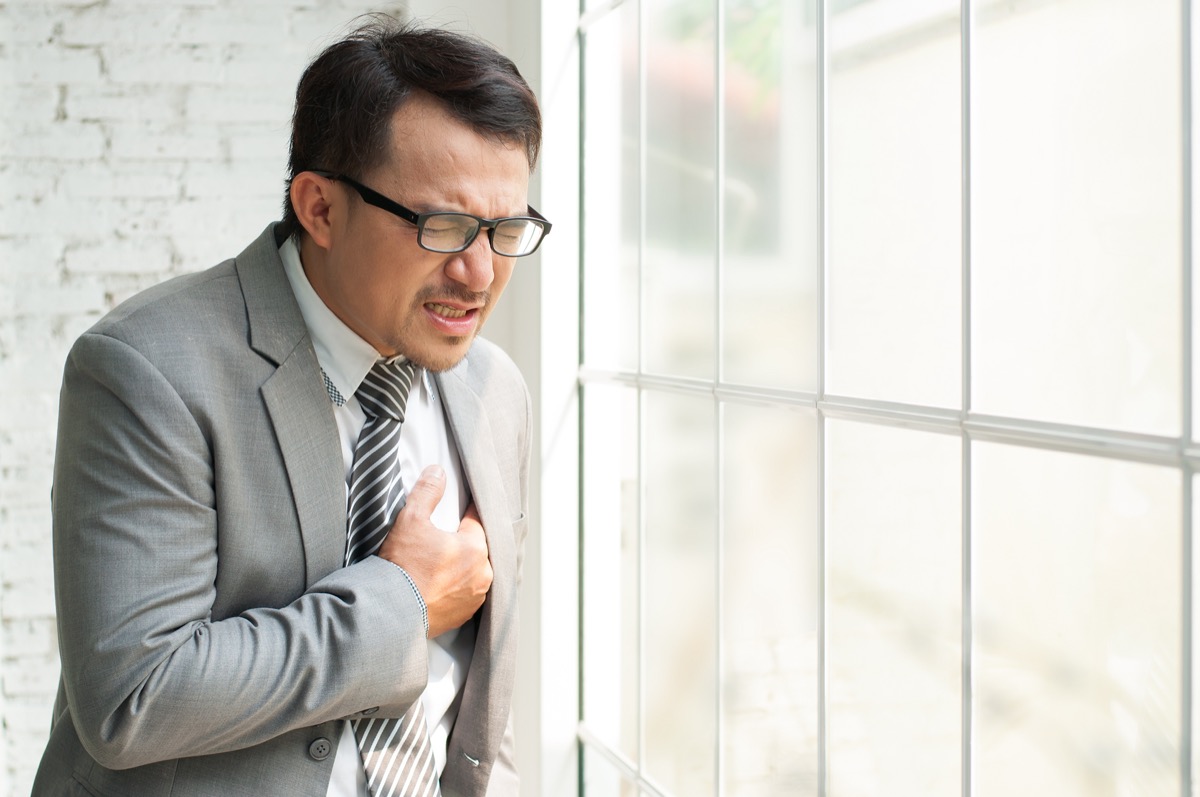 Asian Businessman standing near the window and having chest pain.