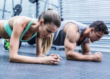 Side view of a muscular couple doing planking exercises