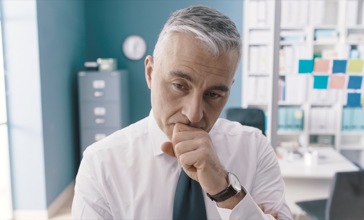 Pensive concerned businessman standing in his office and thinking: business solutions and strategies concept