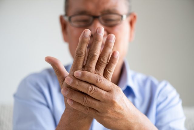 Mature man sitting on sofa and holding his hand.