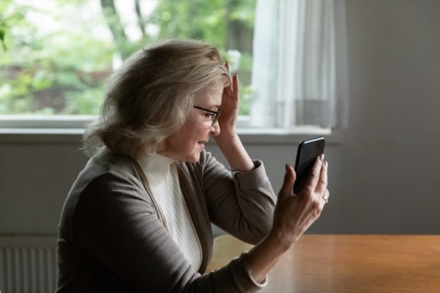 Пенсионер чете съобщение на мобилен телефон