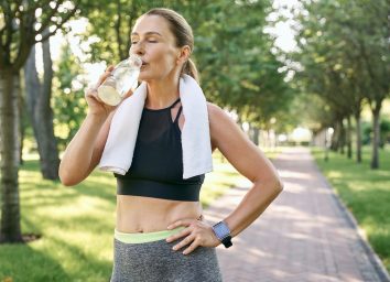 Stay hydrated. Tired fit woman in sportswear refreshing, drinking water after jogging in a green park on a sunny day