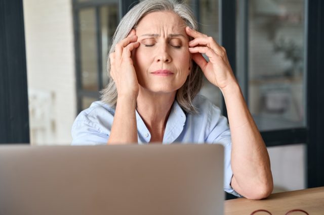 Muncitoare de vârstă mijlocie de 60 de ani stresată care masează capul suferind de dureri de cap la biroul de acasă.
