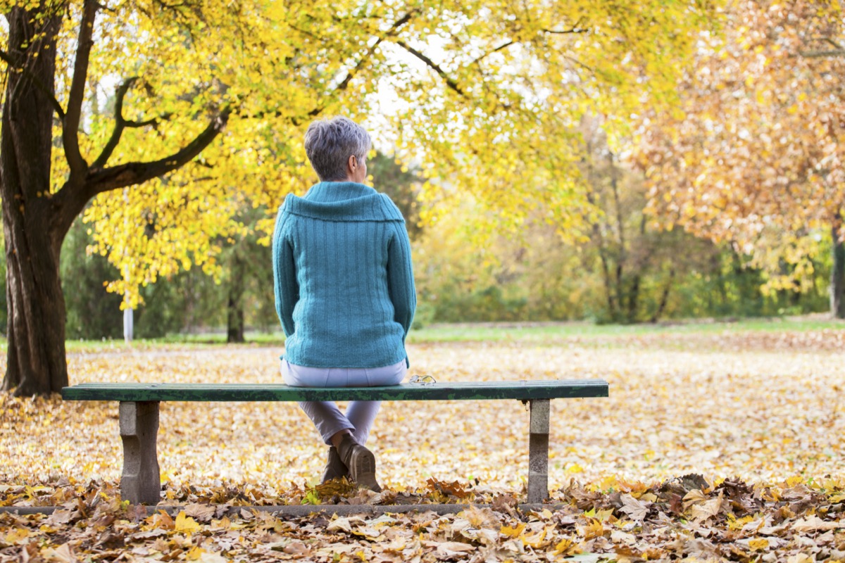 Mature woman on the bench in the autumn garden.