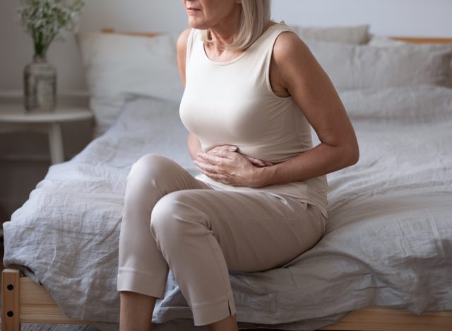 middle aged woman sitting on bed with stomach pain