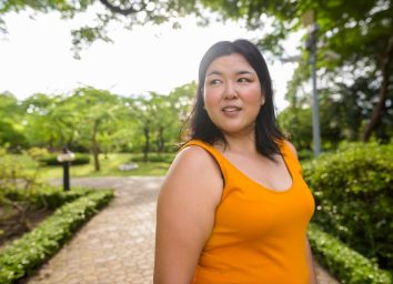 Overweight Asian woman wearing yellow orange dress relaxing in the park.