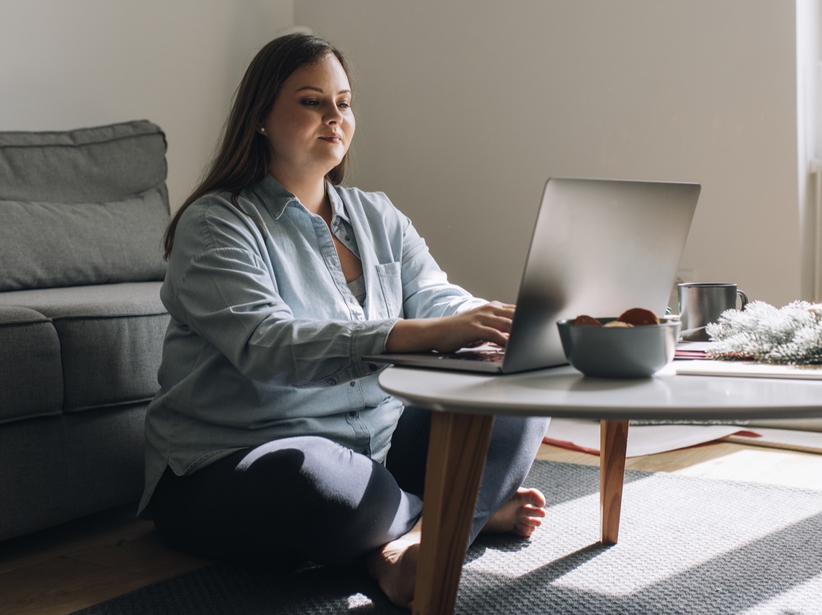 Overweight woman sitting on the floor and using her laptop.