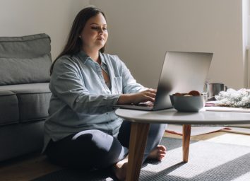 Overweight woman sitting on the floor and using her laptop.