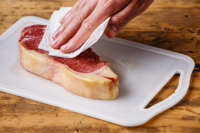 person patting steak with a paper towel