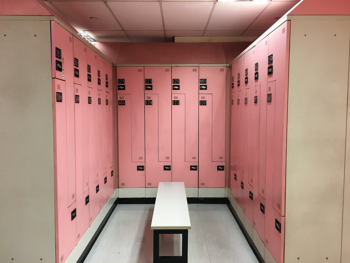 An empty changing room, locker room, dressing room with pink color for female only and thereâ€™s a white bench at the center.