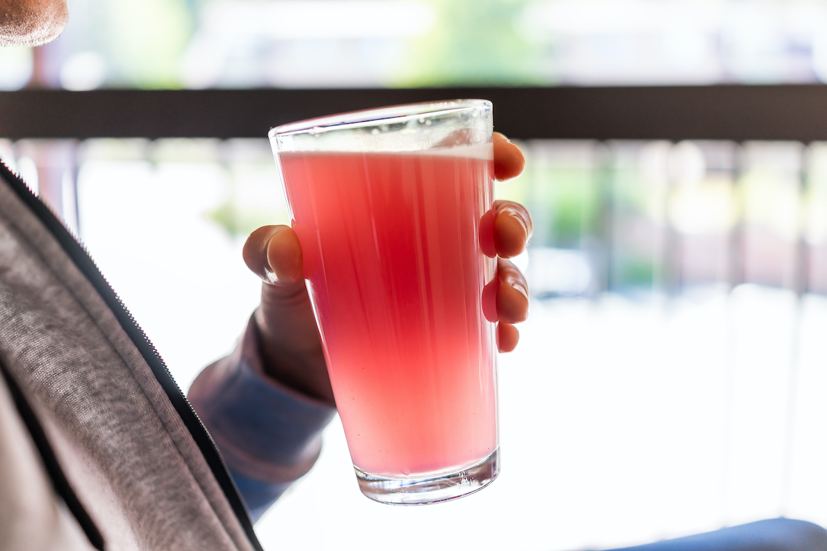 Man sitting outside holding drinking glass of red pink lemonade cocktail juice closeup of drink color