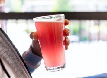 Man sitting outside holding drinking glass of red pink lemonade cocktail juice closeup of drink color