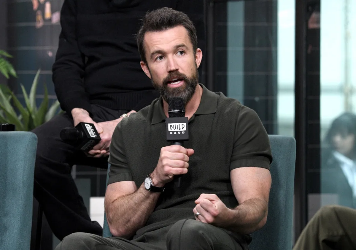 rob mcelhenney in black shirt flexing bicep holding