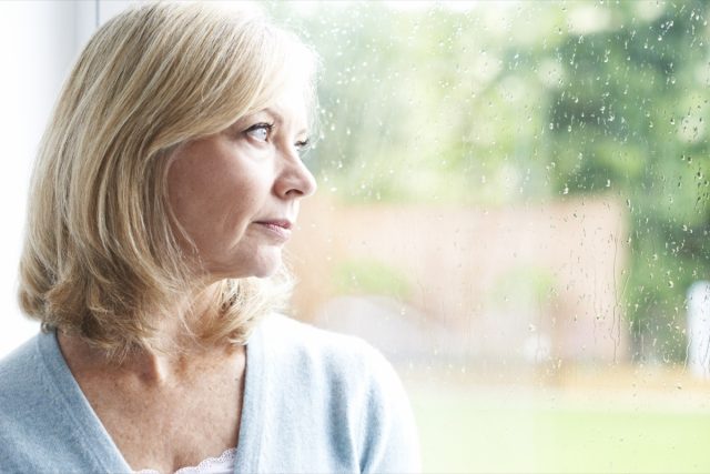 A sad mature woman looks out the window.